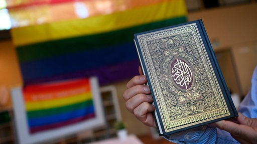 Ein Koran vor einer Prideflagge