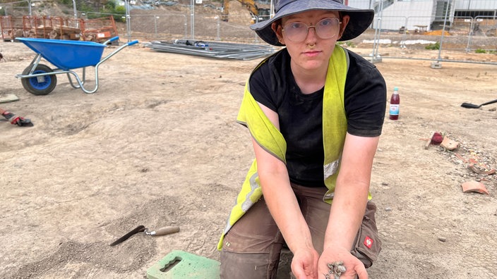 Archäologie-Studentin zeigt ein Armband, das sie bei den Ausgrabungen gefunden hat.