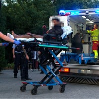 Ein Mann wird auf einer Trage in einen Krankenwagen geschoben. Mehrere Personen stehen um ihn.