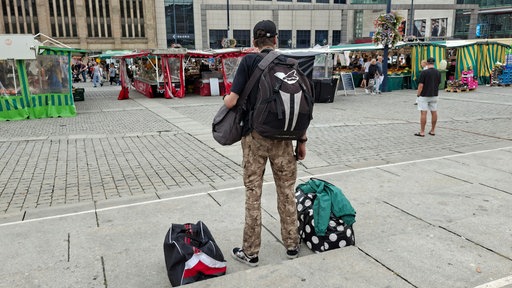 Ein Mann steht mit dem Rücken zur Kamera vor einem Wochenmarkt. 