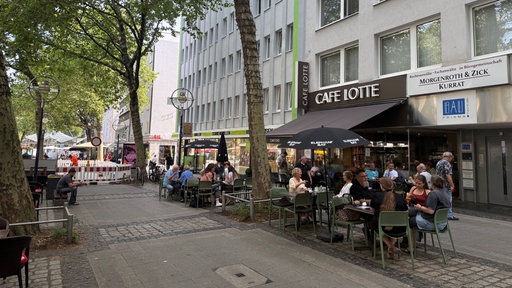 Die Kleppingstraße ist voller Menschen die im Außenbereich der Cafes sitzen.