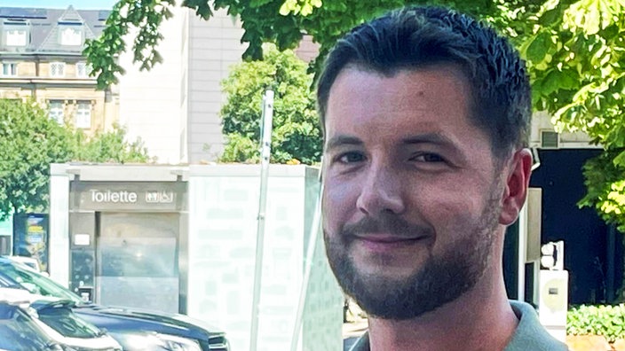 Ein junger Mann mit kurzen Haaren blickt in die Kamera