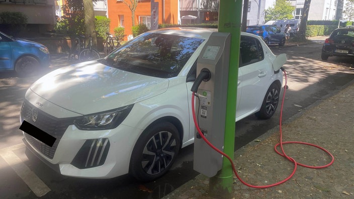 Ein weißes Auto steht neben einer Laterne, an der eine Steckdose ist und lädt per Kabel 
