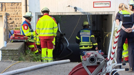 Feuerwehr und Polizei stehen vor einem Haus. Es liegen Feuerwehrschläuche vor dem Haus.