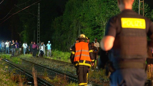 Evakuierte Menschen laufen auf Bahnschienen in Richtung der Hilfskräfte