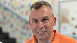 Ein Mann mit einem orangenen Polohemd lächelt in die Kamera.