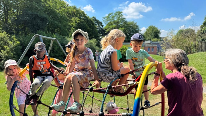 Petra Kern steht neben mehreren Kindern, die auf einem Spielgerät zum Klettern sitzen.