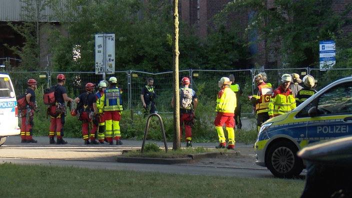 Polizeikräfte in Uniform, zum Teil mit Helm und Kletterausrüstung, an einem Bauzaun