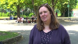 Eine Frau mit dunklen Haaren sitzt auf einem Schulhof und schaut in die Kamera.