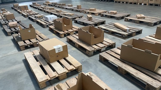 In einer Lagerhalle liegen mehrere Paletten mit Paketen herum.