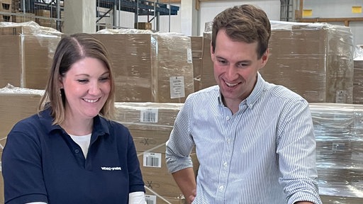 Ein Mann und eine Frau in einer Lagerhalle blicken auf ein Notebook
