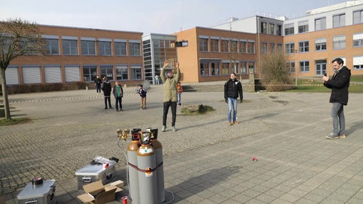 Mehrere Schüler auf dem Pausenhof, ein Bereich ist abgesperrt, ein Mann lässt gerade einen großen Ballon steigen