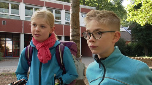 Ein Junge und ein Mädchen sitzen vor einem Baum auf einem Schulhof