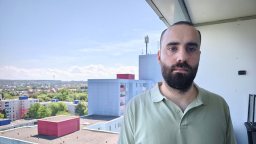 Mann steht auf Balkon im Hochhaus.