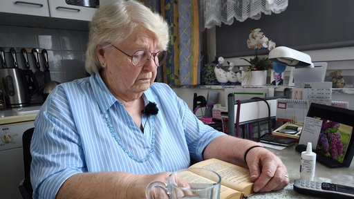 Ältere Frau sitzt in ihrer Wohnung und liest.