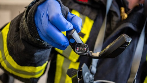 Eine Person von der Feuerwehr zeigt einen kleinen Bildschirm, der in eine Atemschutzmaske eingesetzt werdne kann.