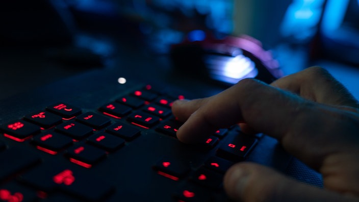 Eine Tastatur die rot läuchtet und auf der eine Hand die Tasaten berührt. Der Hintergrund ist dunkel und nur die Tasatatur ist im Fokus.