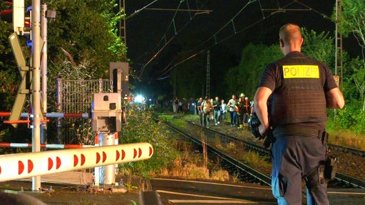 Nächtlicher Einsatz an Bahngleisen: Ein Polizist beobachtet am Bahnübergang, wie Fahrgäste über die Gleise evakuiert werden.