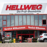 Zu sehen ist der Eingang einer Hellweg-Filiale, ein Mann räumt Einkäufe in sein Auto.
