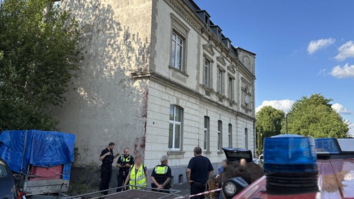 Polizei und Anwohner halten sich vor dem geräumten Mehrfamilienhaus auf