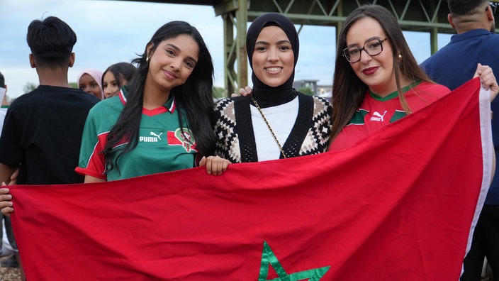 Drei Frauen stehen mit Marokko-Flagge vor der Leinwand im Hafengarten