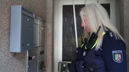 Eine Bezirksbeamtin der Polizei steht in einem Hauseingang und schaut auf die Klingelschilder