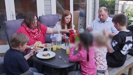 Eine große Familie sitzt im Garten an einem Tisch und isst gemeinsam.