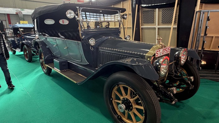 Ein sehr altes, dunkelblaues Auto in der Form einer Kutsche mit goldenen Verzierungen.