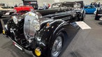 Ein schwarzer Oldtimer mit glänzendem Lack in einer Messehalle.
