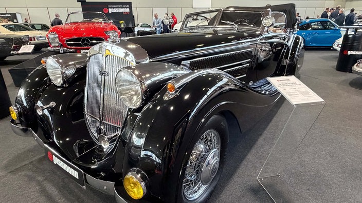 Ein schwarzer Oldtimer mit glänzendem Lack in einer Messehalle.