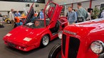 Ein glänzend-roter Lamborghini-Sportwagen mit nach oben aufgeklappten Türen, daneben ein Lamborghini-Traktor mit dem gleichen Lack.