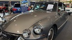 Ein Oldtimer mit glänzend-grauem Lack in einer Messehalle.