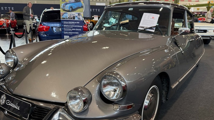 Ein Oldtimer mit glänzend-grauem Lack in einer Messehalle.