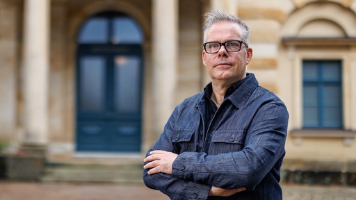 Marcus Lobbes steht in einem blauen Anzug vor einem Jugendstil-Gebäude.