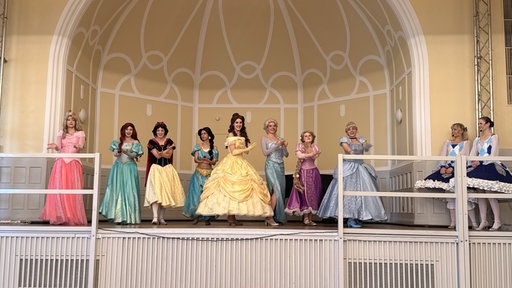 Mehrere Frauen, verkleidet als Disneyprinzessinnen, stehen auf einer Bühne.