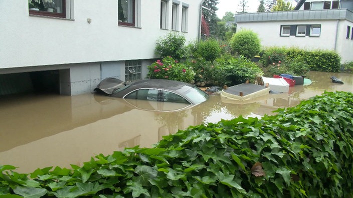 Ein mit Wasser überfluteter Garten, ein Auto ist fast untergegangen
