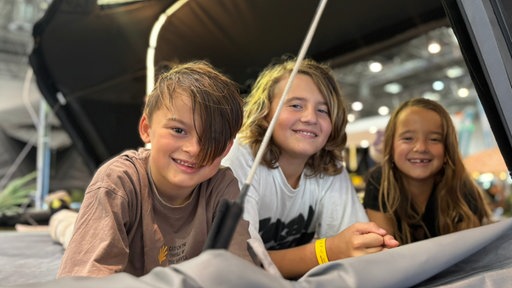 Drei Kinder liegen in einem Dachzelt und lächeln in die Kamera