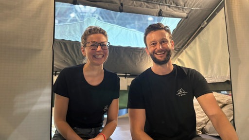 Ein Mann und eine Frau in schwarzen T-Shirts sitzen in einem Dachzelt