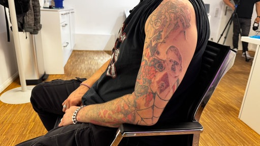 Ein Mann sitzt quer auf dem Stuhl und hat Nazi-Tattoos
