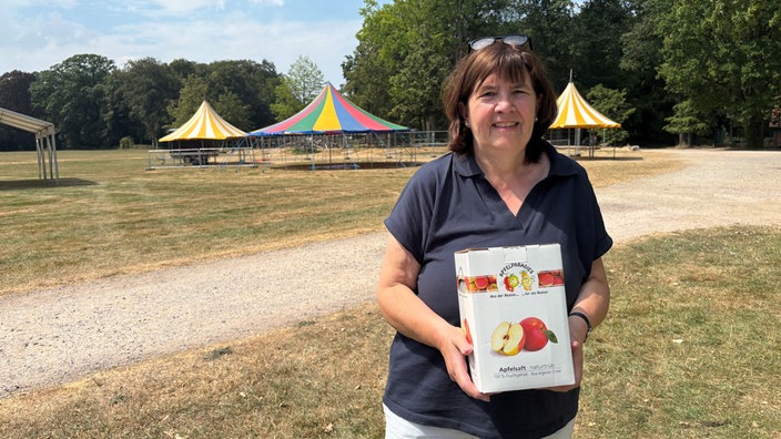 Eine Frau steht auf einem Feld und hält eine Kiste Apfelsaft in den Händen