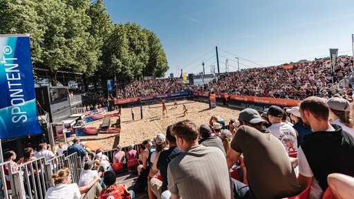 Volle Zuschauertribünen und ein Beachvolleyball-Feld in der Mitte