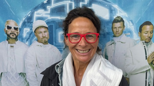 Frau posiert vor einer Fotowand; links und rechts von ihr sind jeweils 2 Mitglieder der Backstreet Boys abgebildet.