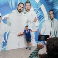 Person posiert mit ausgebreitreten Armen vor Fotowand. Fotowand zeigt Member der Backstreet- Boys.