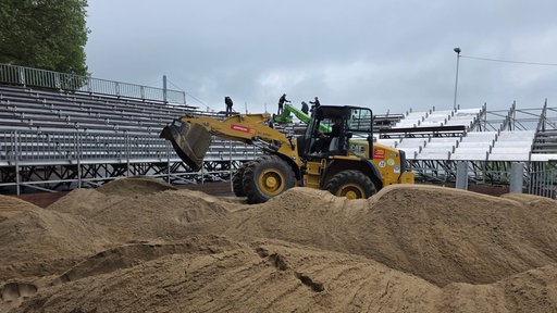 Am Düsseldorfer Rheinufer wird der Sand für die German Beach Tour aufgeschüttet - ein Bagger hilft dabei.