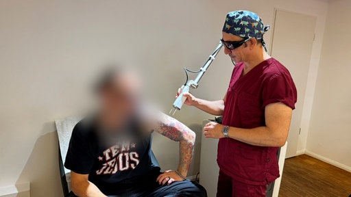 Arzt hat ein Lasergerät in der Hand und entfernt Tattoos von Ex-Neo-Nazi