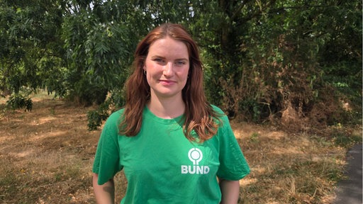 Julia Stratmann vom BUND NRW ist im Porträt zu sehen. Sie trägt ein grünes T-Shirt und steht vor Pflanzen im Hintergrund.