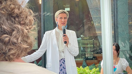 Eine Frau steht vor einem Publikum und hält eine Rede.