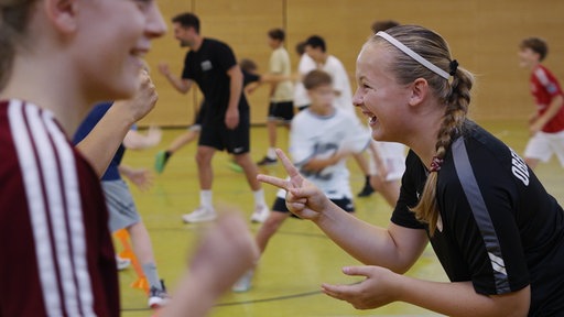 Sporthalle in einer Schule. Kinder laufen herum.
