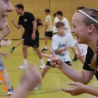 Sporthalle in einer Schule. Kinder laufen herum.