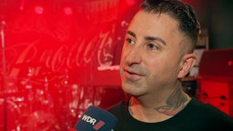 Ein Mann spricht in ein Mikrofon mit WDR-Logo.